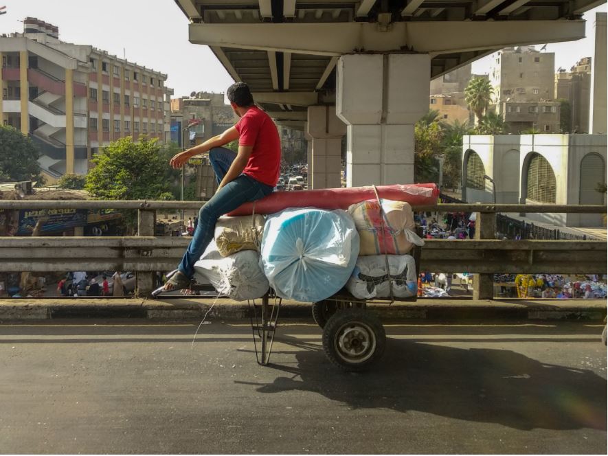 شاب يجلس على عربة تحمل سجادًا