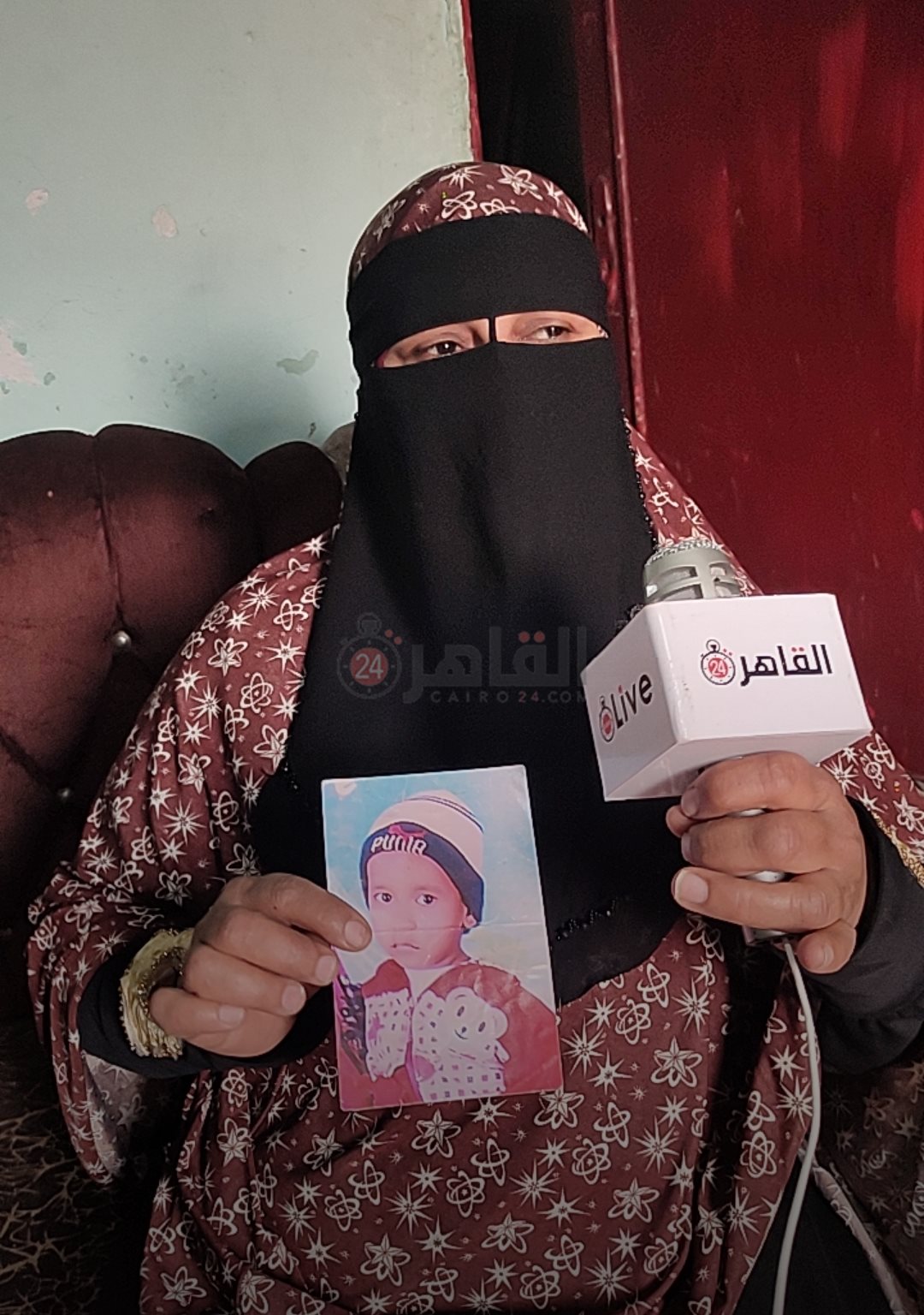 الأم تمسك بصورة طفلها أثناء حديثها لـ القاهرة 24