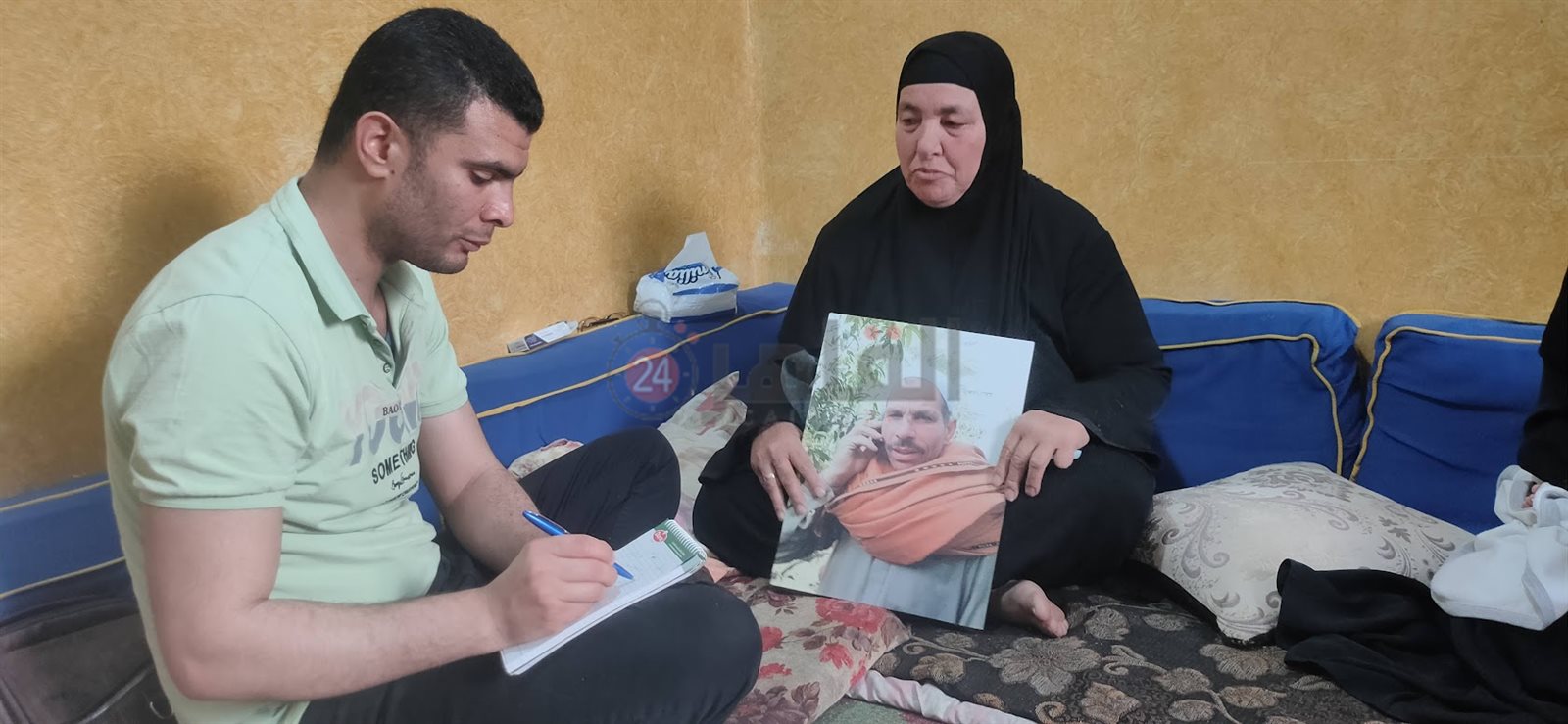 زوجة المجني عليه تمسك بصورته اثناء حديثها لـ القاهرة 24