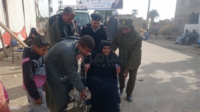 فرد شرطة يساعد مسنة تجلس على كرسي متحرك للإدلاء بصوتها في انتخابات رئاسة الجمهورية بقنا | صور