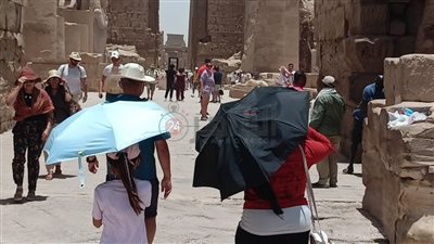 السياح بمعبد الكرنك يتحدون الموجة الحارة في الأقصر بالشمسية والقبعات